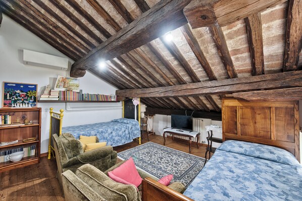 A cozy attic bedroom with exposed wooden beams, a bed, a sofa, a small table, and a bookshelf.