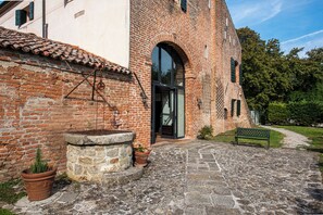 Une cour avec un bâtiment en briques, un puits en pierre et un banc.