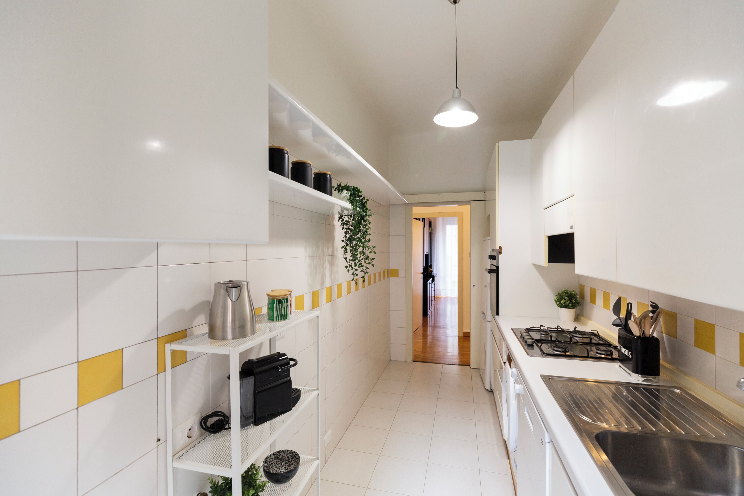 A modern kitchen with white cabinets, a stainless steel sink, and a yellow and white tiled backsplash.