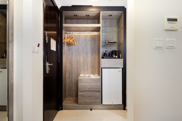 A compact kitchen with a built-in refrigerator, a small countertop, and a wooden cabinet with hanging clothes. - Alayam Elite Hotel (Makkah)