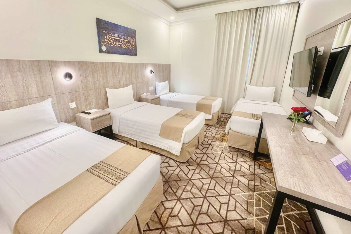 A hotel room with three beds, a desk, a TV, and a large mirror.