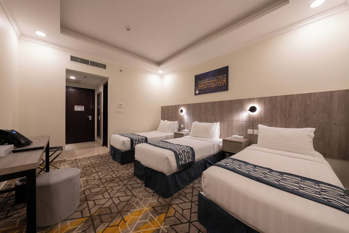 A hotel room with two beds, a desk, a chair, and a small table.