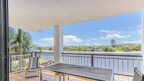 A balcony with a table and benches, overlooking a river and greenery.