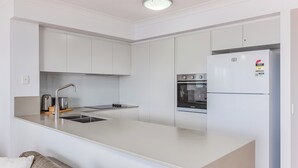 Una cocina moderna con armarios blancos, horno empotrado y refrigerador.