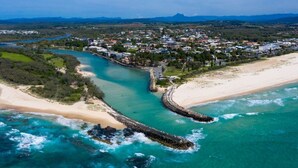 Vista aérea de un pueblo costero con playa, río y un puente que conecta la tierra con el agua.