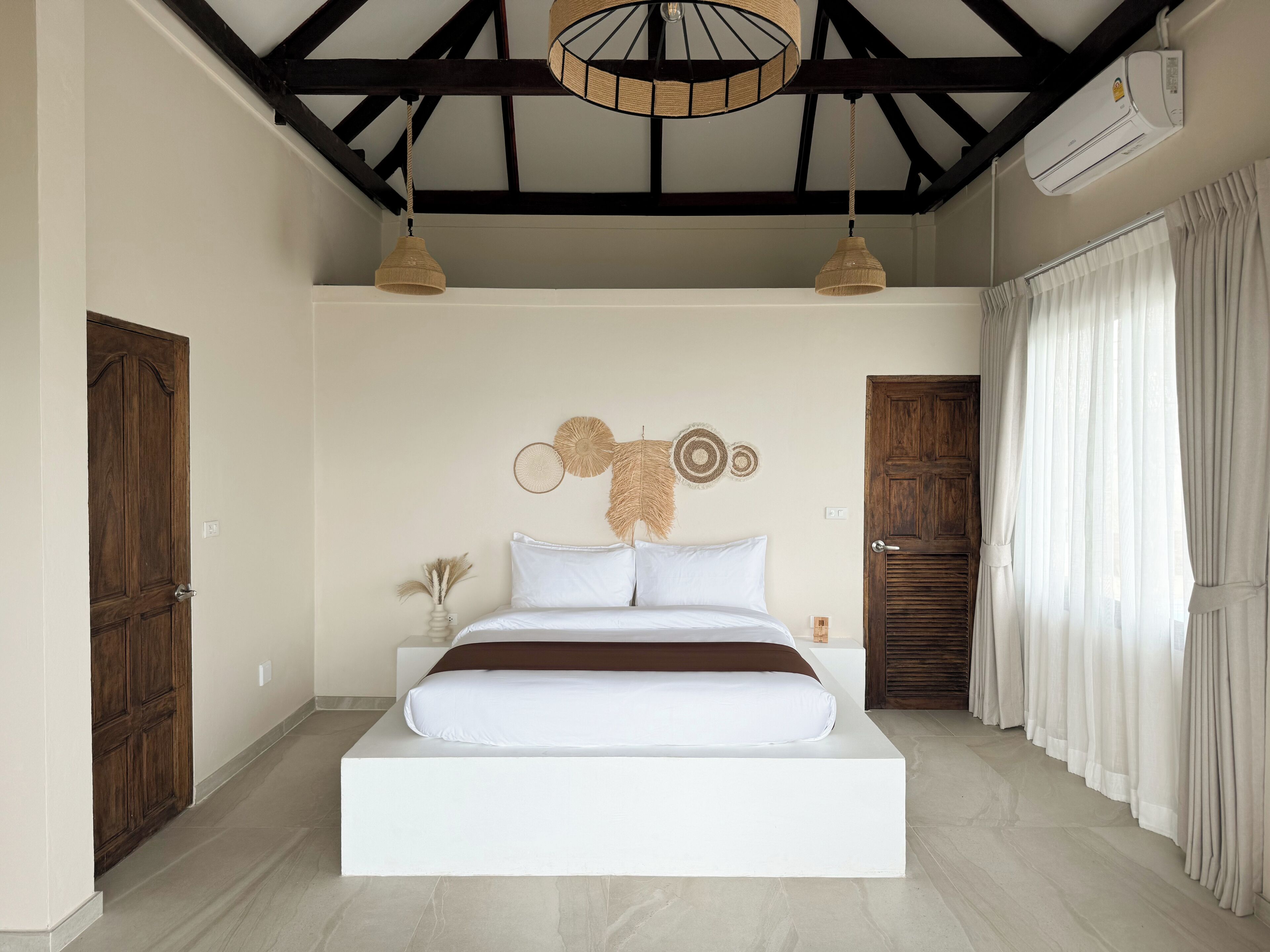 A modern bedroom with a large bed, wooden doors, a ceiling fan, and a large window with curtains.