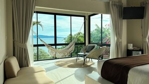 A bedroom with a large window, a hammock, a bed, and a chair.