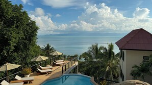 A poolside area with lounge chairs and umbrellas, overlooking a large body of water and distant mountains.