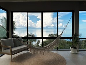 Una hamaca en una habitación con ventanas amplias que dan a un cuerpo de agua y montañas.