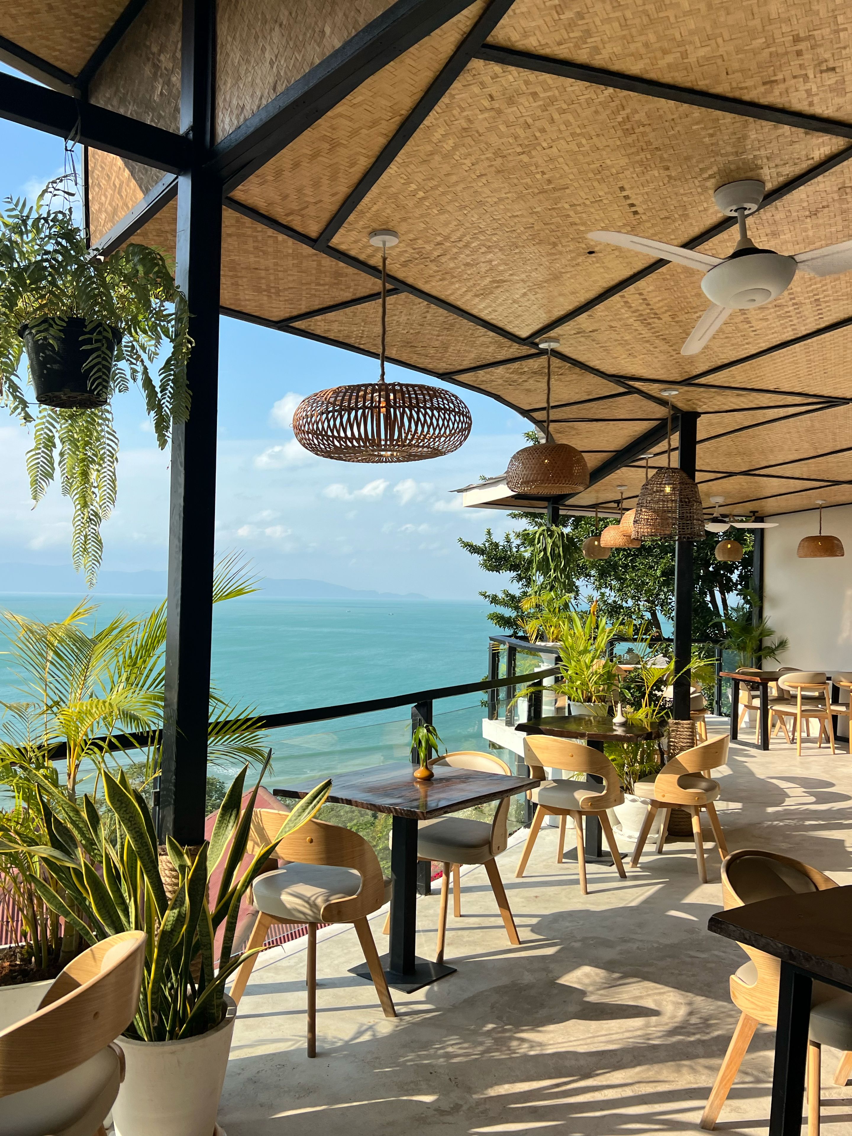 Un espacio al aire libre con mesas, sillas, ventilador de techo y plantas colgantes.