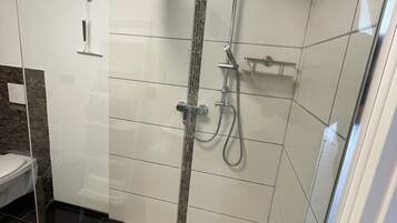 Un baño moderno con cabina de ducha de vidrio, paredes de azulejos blancos y suelo negro.
