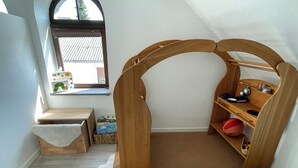 Ein gemütliches Zimmer mit einem hölzernen Spielhaus, einem kleinen Tisch und einem Fenster mit Aussicht.