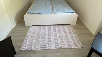 Ein kleines, helles Zimmer mit einem Einzelbett, einem gemusterten Teppich und zwei Stühlen.