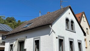 Ein weißes Gebäude mit einem Ziegeldach, zahlreichen Fenstern und einer kleinen Treppe zum Eingang.