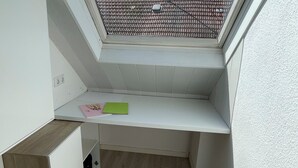 Ein kleiner, abgeschlossener Balkon mit einer geneigten Dachkonstruktion, einer weißen Wand und einem Holzboden.