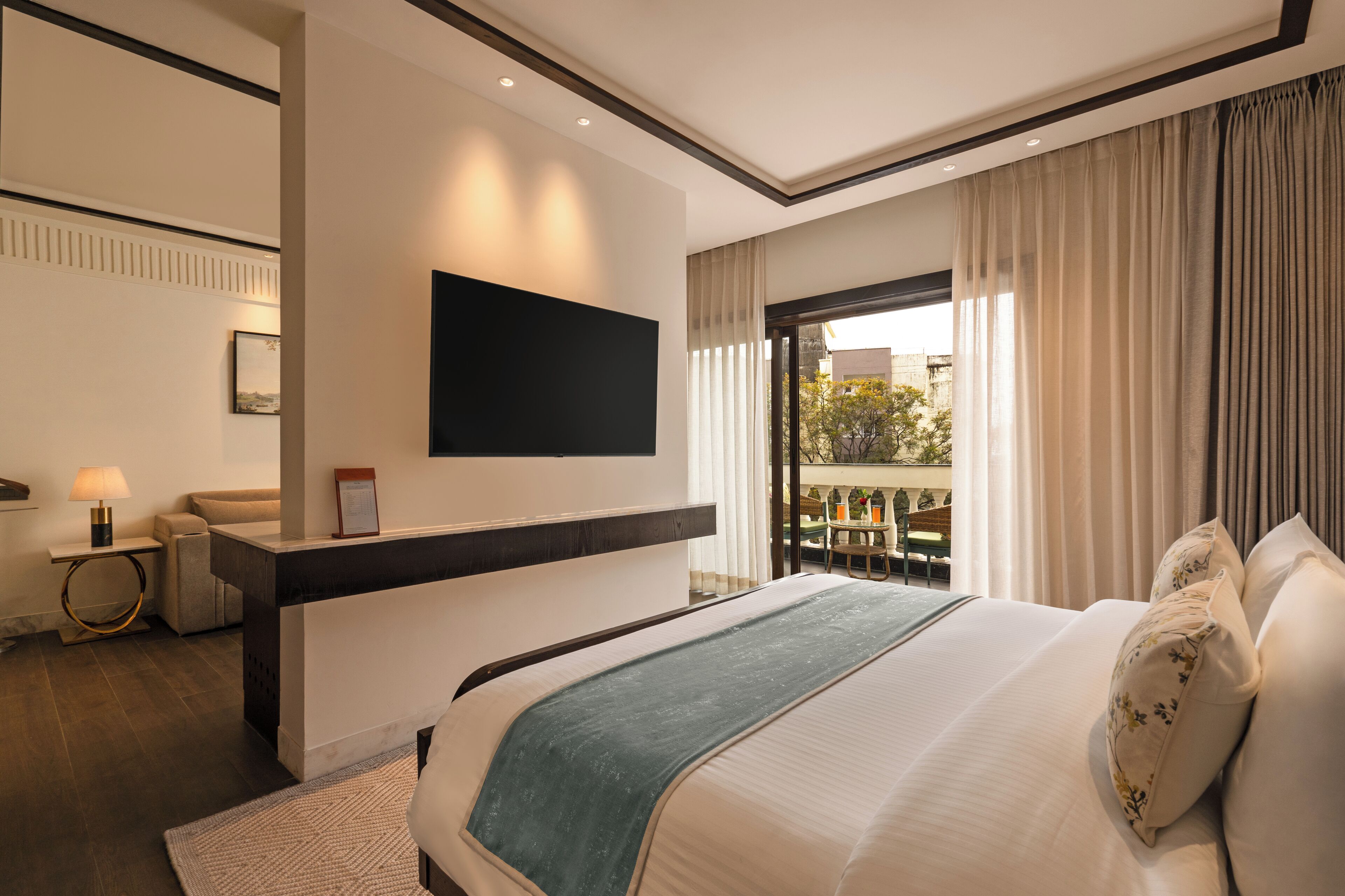 Une chambre d’hôtel moderne dotée d’un grand lit, d’un téléviseur à écran plat fixé au mur, d’un balcon avec vue et d’un petit coin salon avec une table et des chaises.
