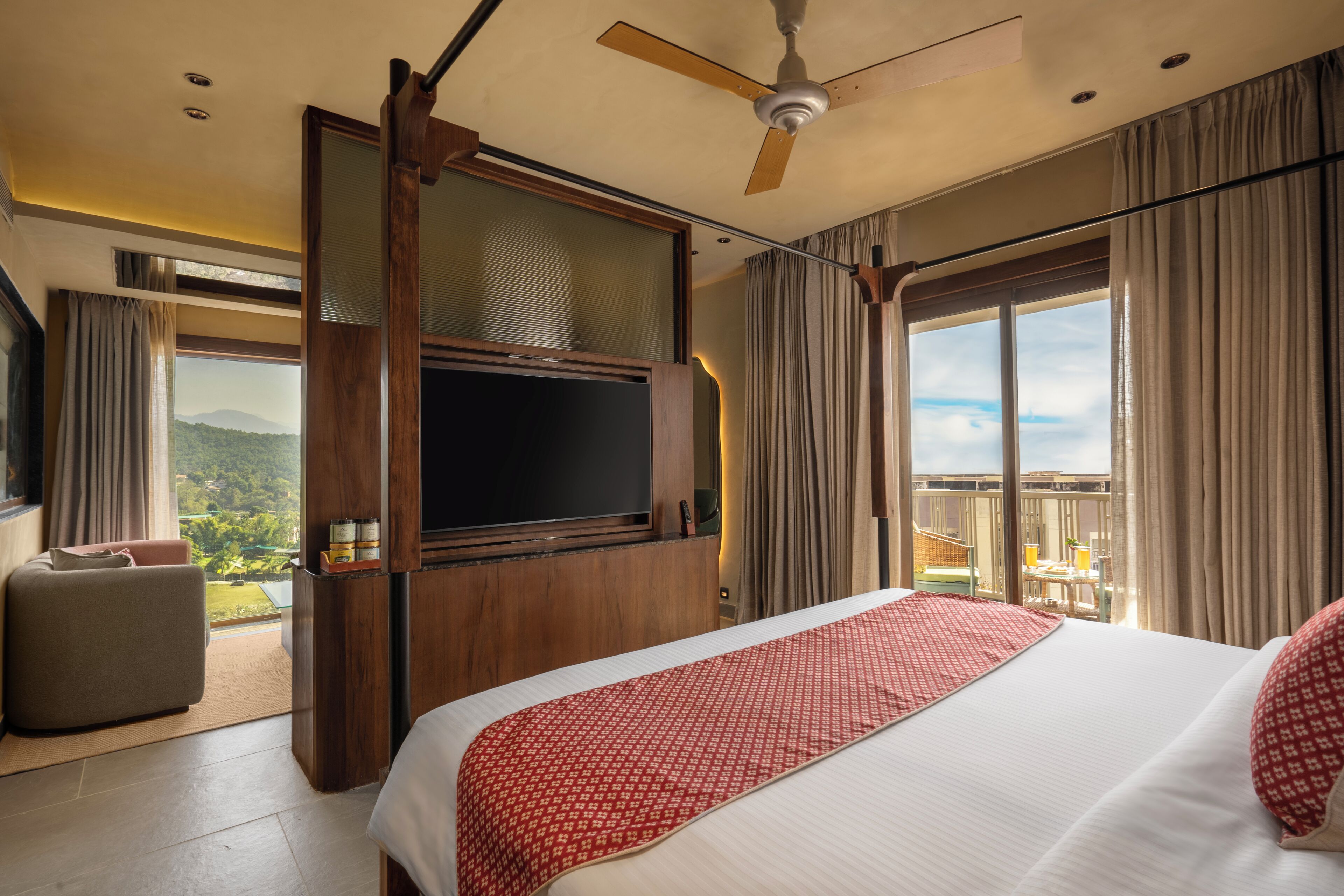 Een hotelkamer met een groot bed, een televisie, een balkon met uitzicht op de bergen en een plafondventilator.