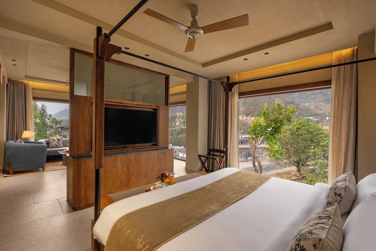 A hotel room with a large bed, a TV, a balcony with a view of the city, and a ceiling fan.