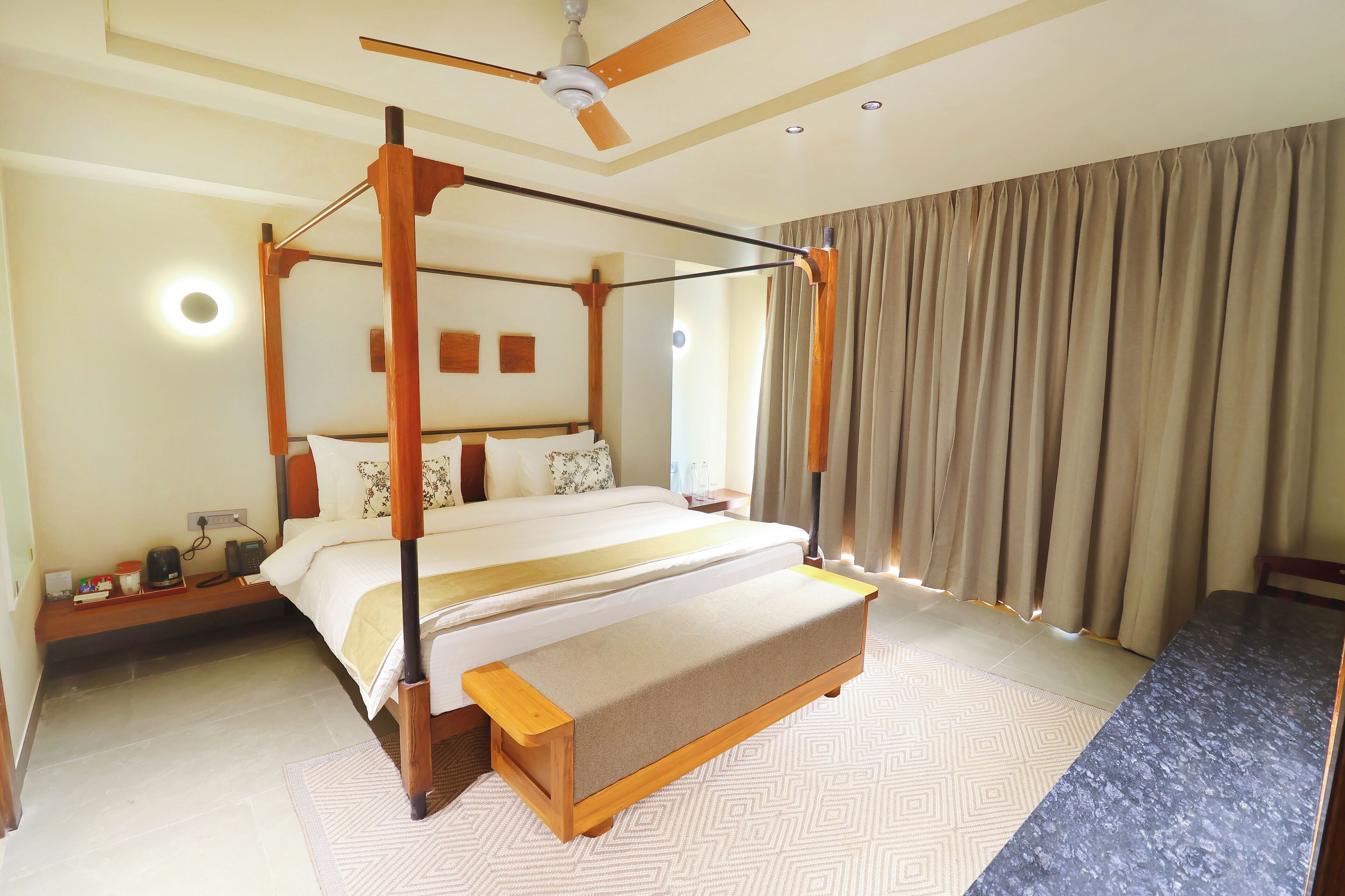 A four-poster bed with a bench, a ceiling fan, and a large window with curtains.