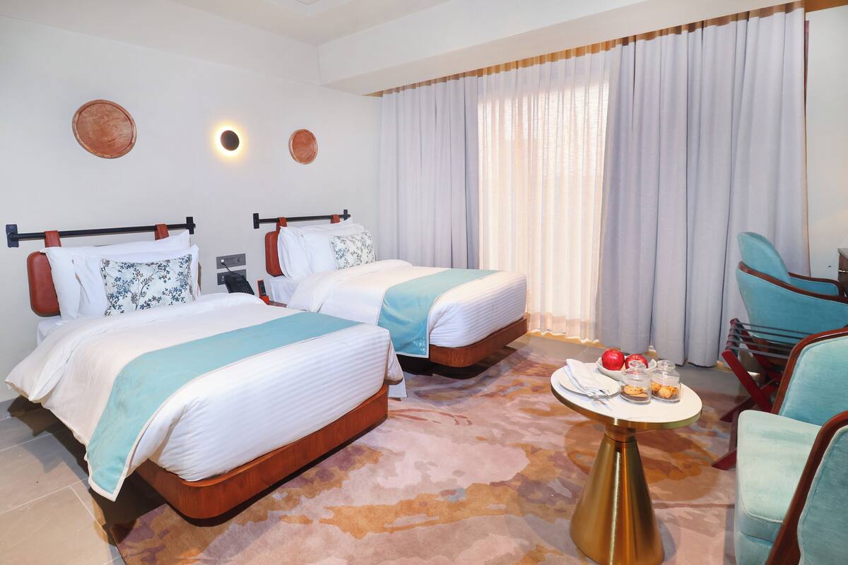 A hotel room with two beds, a round table with a tray of snacks, and a chair.