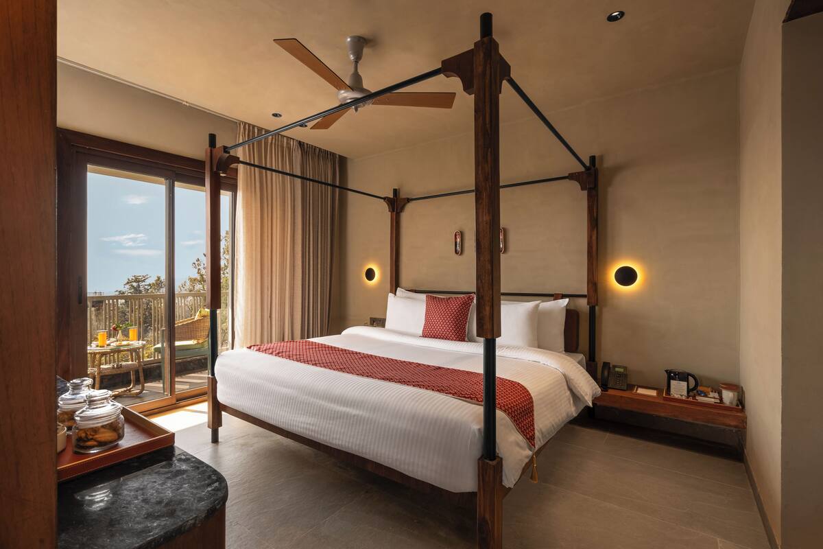 A four-poster bed with a canopy, a nightstand with a lamp, and a view of the outdoors through a sliding glass door.