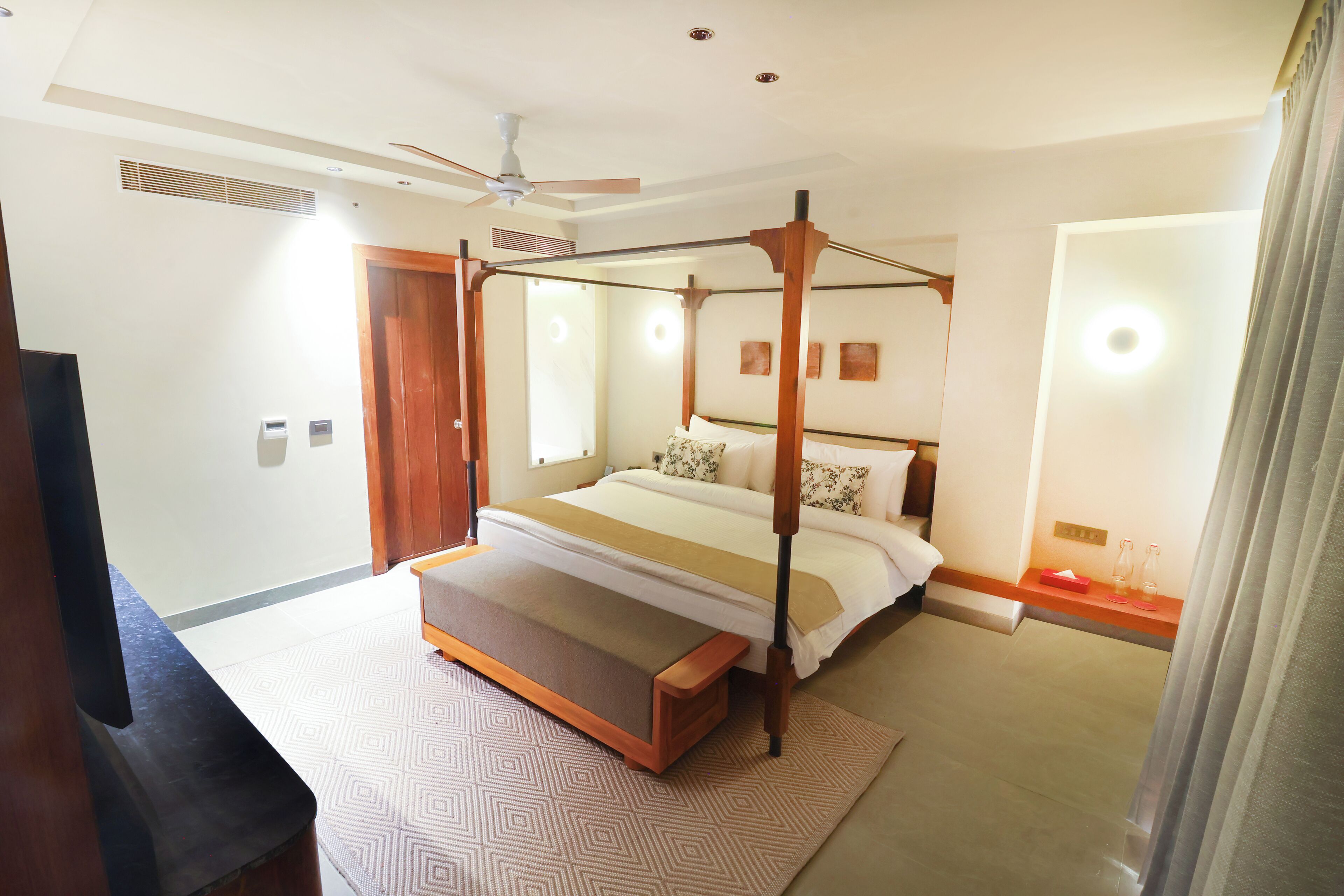A modern bedroom with a four-poster bed, a ceiling fan, and a bedside table with a lamp.