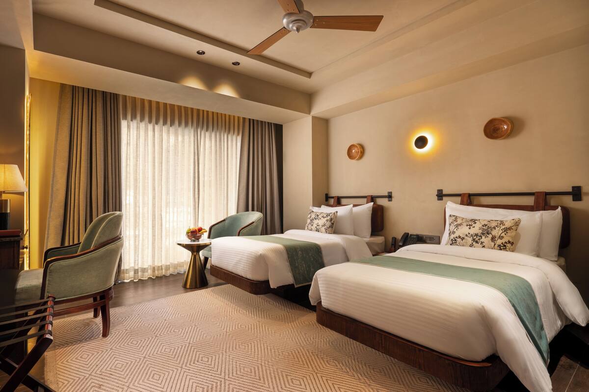 A hotel room with two beds, a desk, a chair, and a ceiling fan.