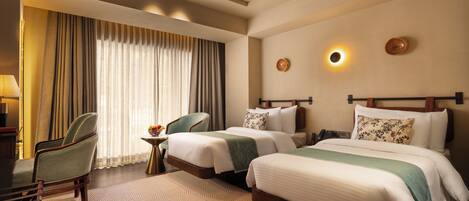 A hotel room with two beds, a desk, a chair, and a ceiling fan.