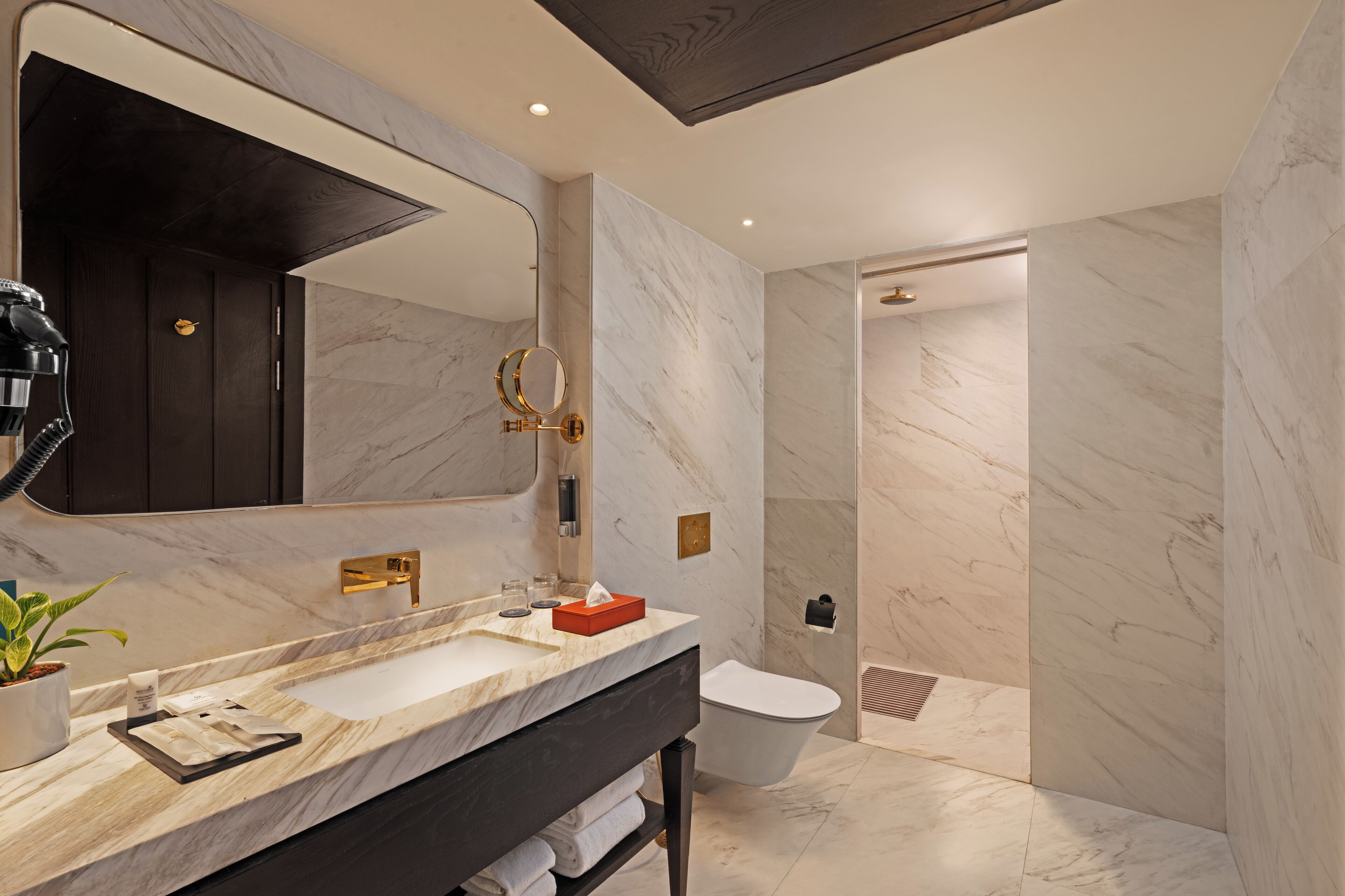 A modern bathroom with a marble vanity, a large mirror, a toilet, and a shower area.