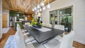 Een moderne keuken met een centraal eiland, witte eetkamerstoelen en een donker houten tafel.