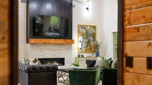 Een gezellige woonkamer met een open haard, leren banken, een groene fauteuil en een groot schilderij aan de muur.