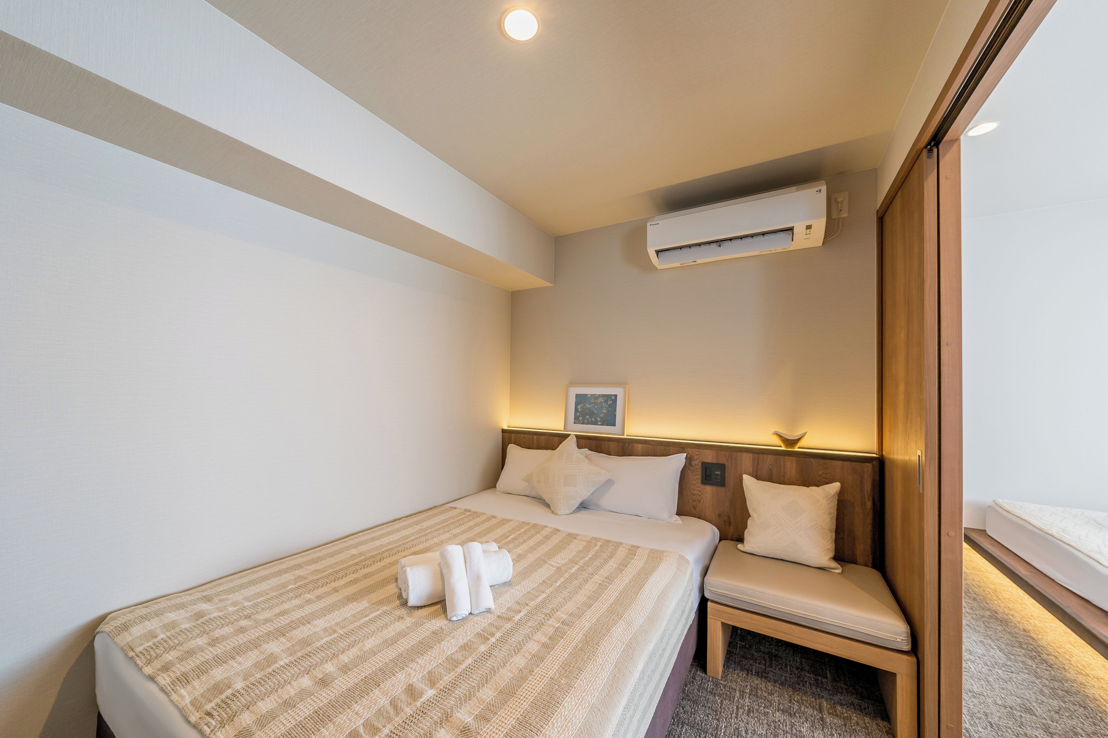 Ein Hotelzimmer mit Bett, Nachttisch, Stuhl, Klimaanlage und einem Bild an der Wand.