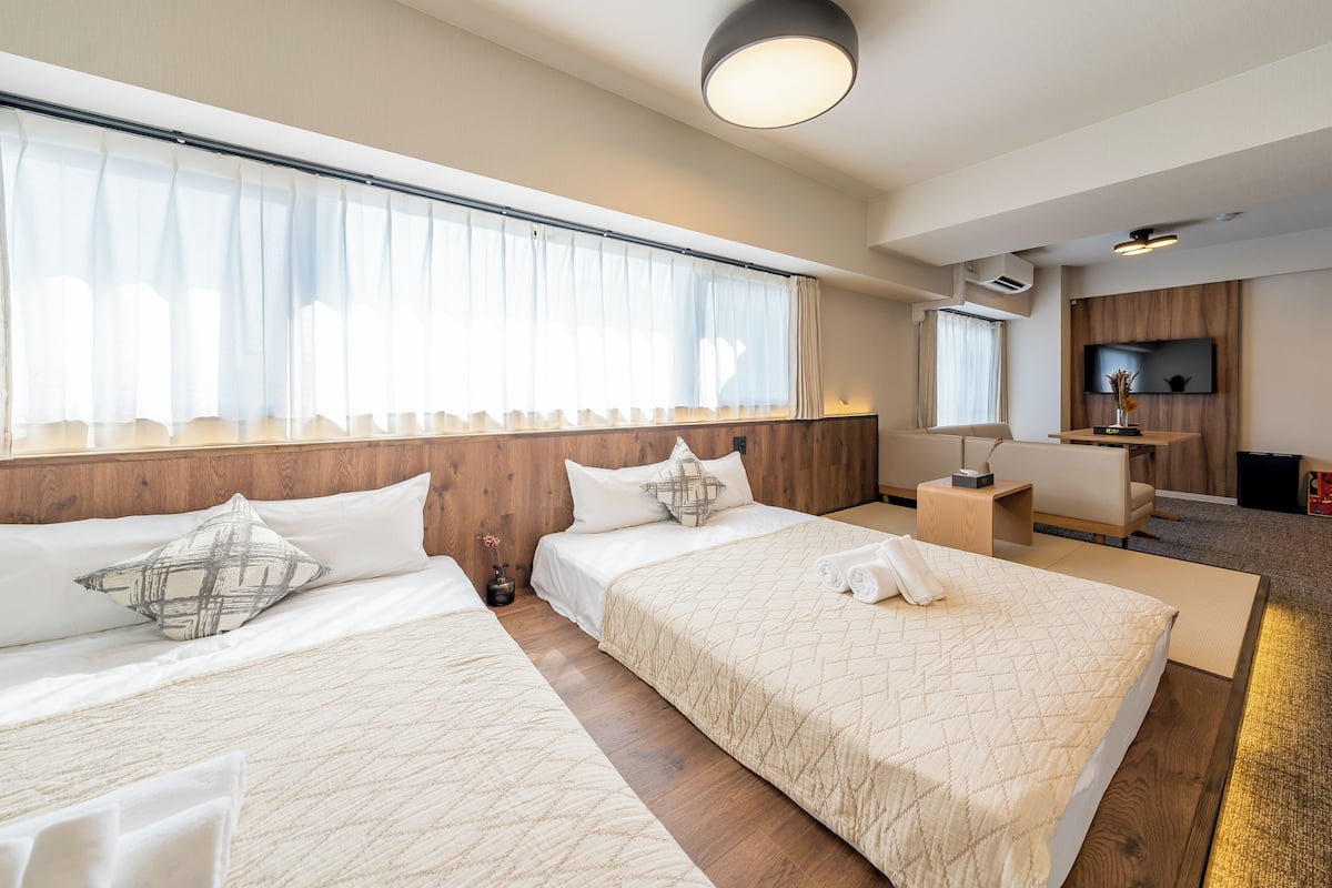 Une chambre d’hôtel avec deux lits, un bureau, une télévision et une grande fenêtre avec des rideaux légers.