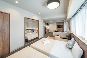 Een moderne hotelkamer met twee bedden, een zithoekje, een kitchenette en een groot raam met gordijnen.