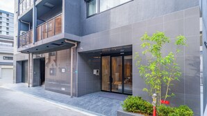 Un bâtiment moderne à la façade grise, doté d’une entrée en verre et d’un petit arbre en premier plan.