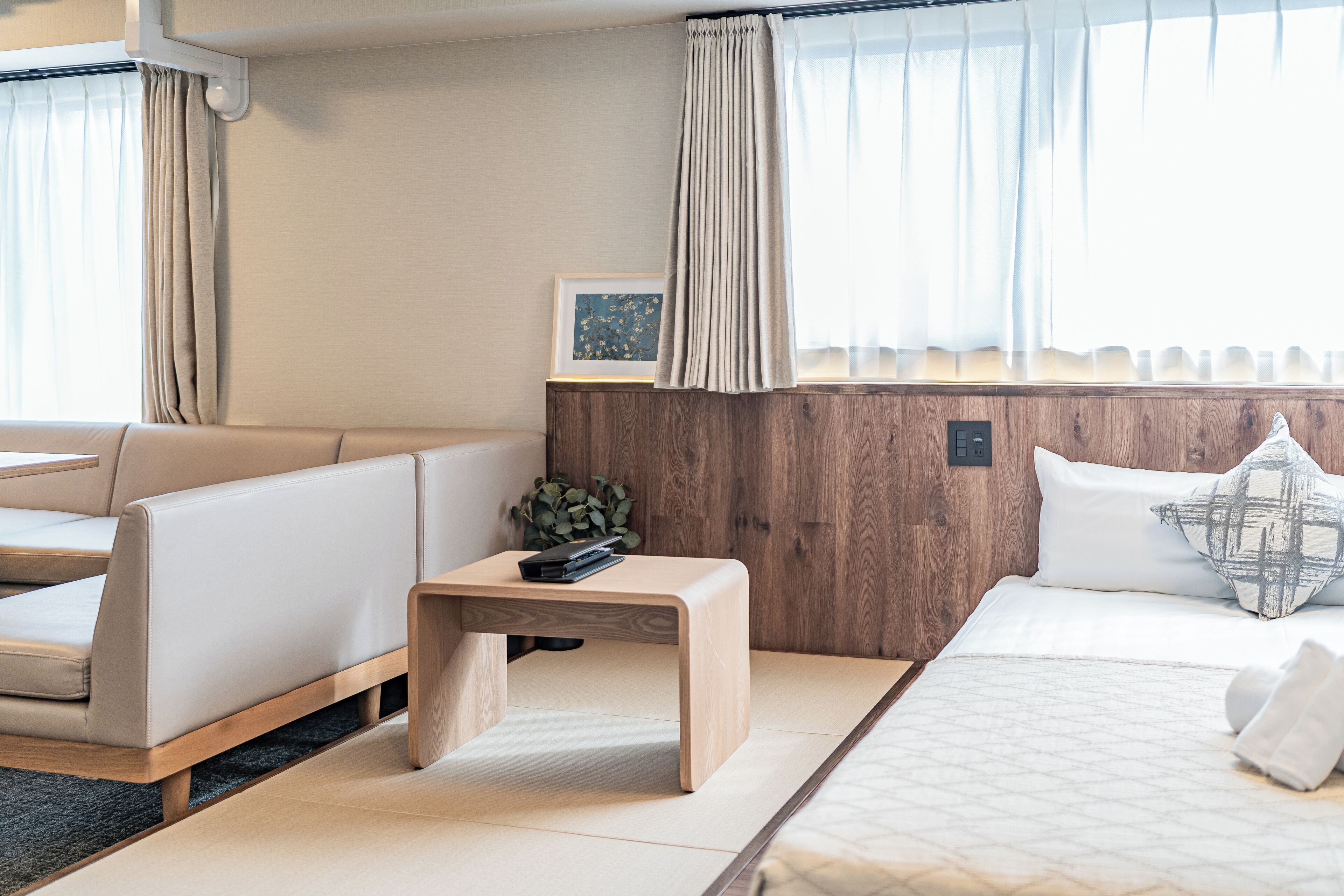 A modern hotel room with a bed, a sofa, a wooden nightstand, and a framed picture on the wall.