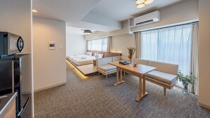 Une chambre d’hôtel moderne dotée d’une kitchenette, d’un canapé-lit, d’une table à manger et d’une grande fenêtre avec des rideaux.