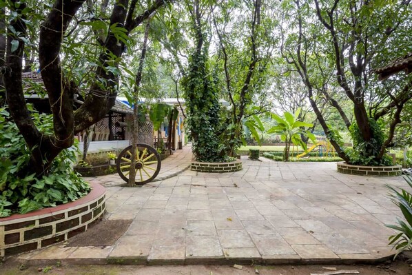 Un sendero pavimentado rodeado de exuberante vegetación y una noria grande de madera.