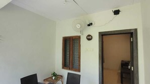 Ein Zimmer mit Esstisch und Stühlen, einem Fenster mit Jalousien, einer Wanduhr und einer Tür zu einem anderen Raum.