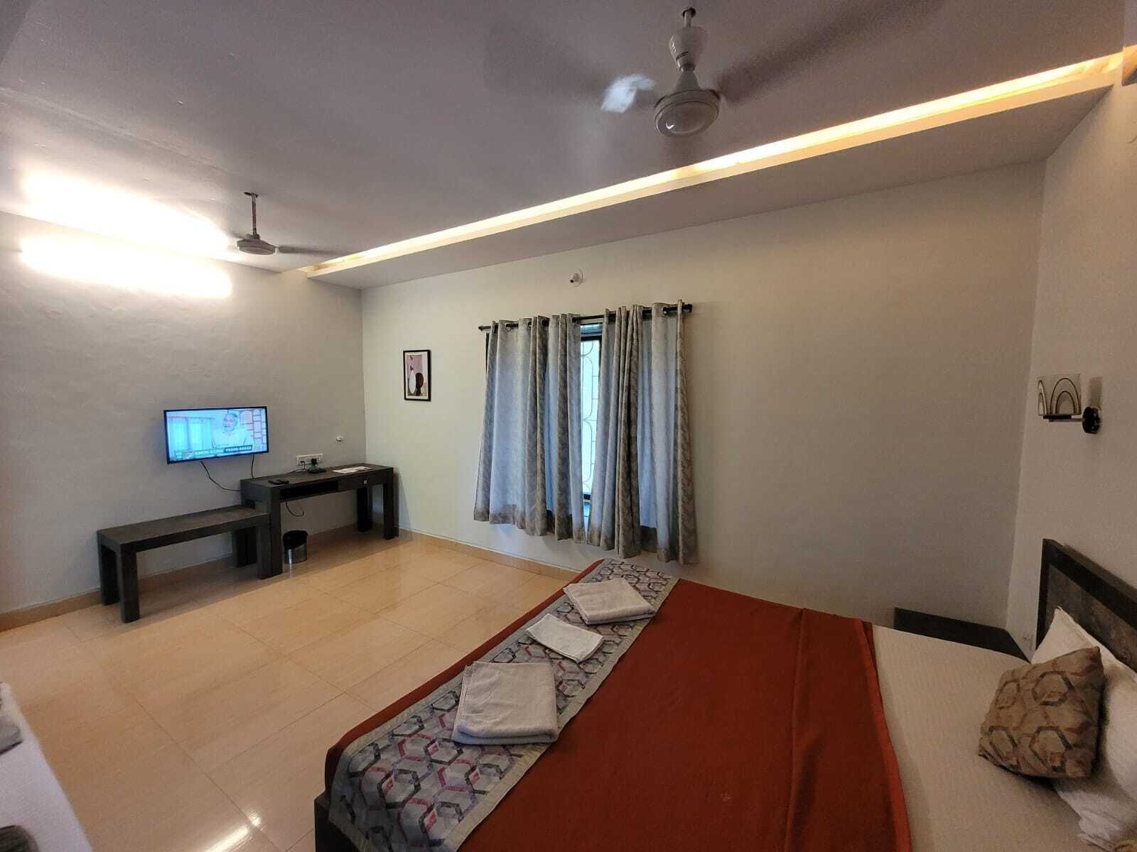 Una habitación de hotel con cama, escritorio, televisión y ventana con cortinas.