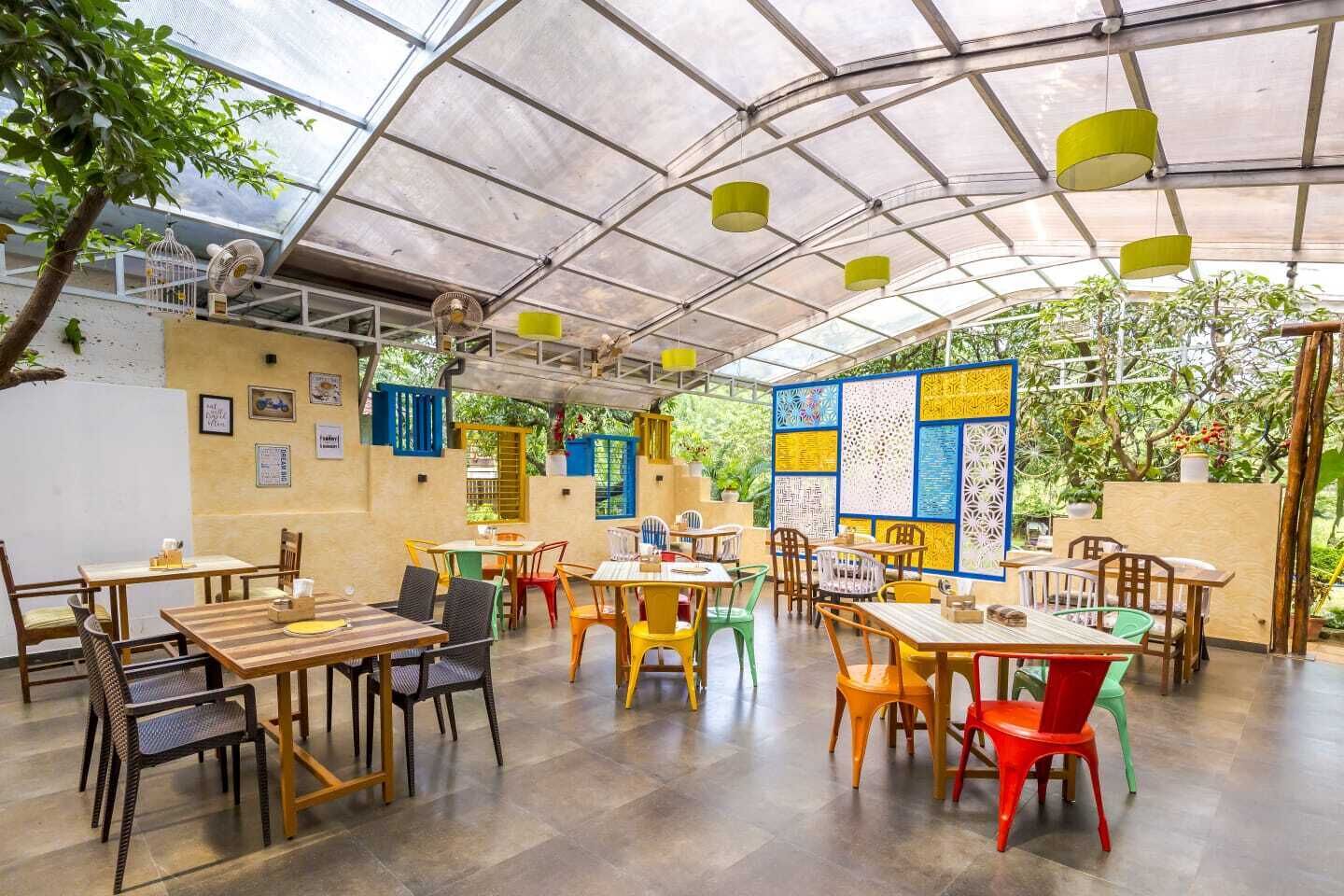 Ein überdachter Außenbereich zum Essen mit Tischen und Stühlen, einer Tafel an der Wand und Kübelpflanzen.