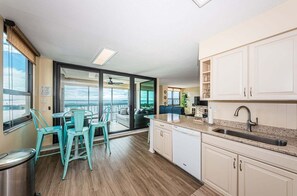 A modern kitchen with a large window, a dining area with teal chairs, and a view of the outdoors.