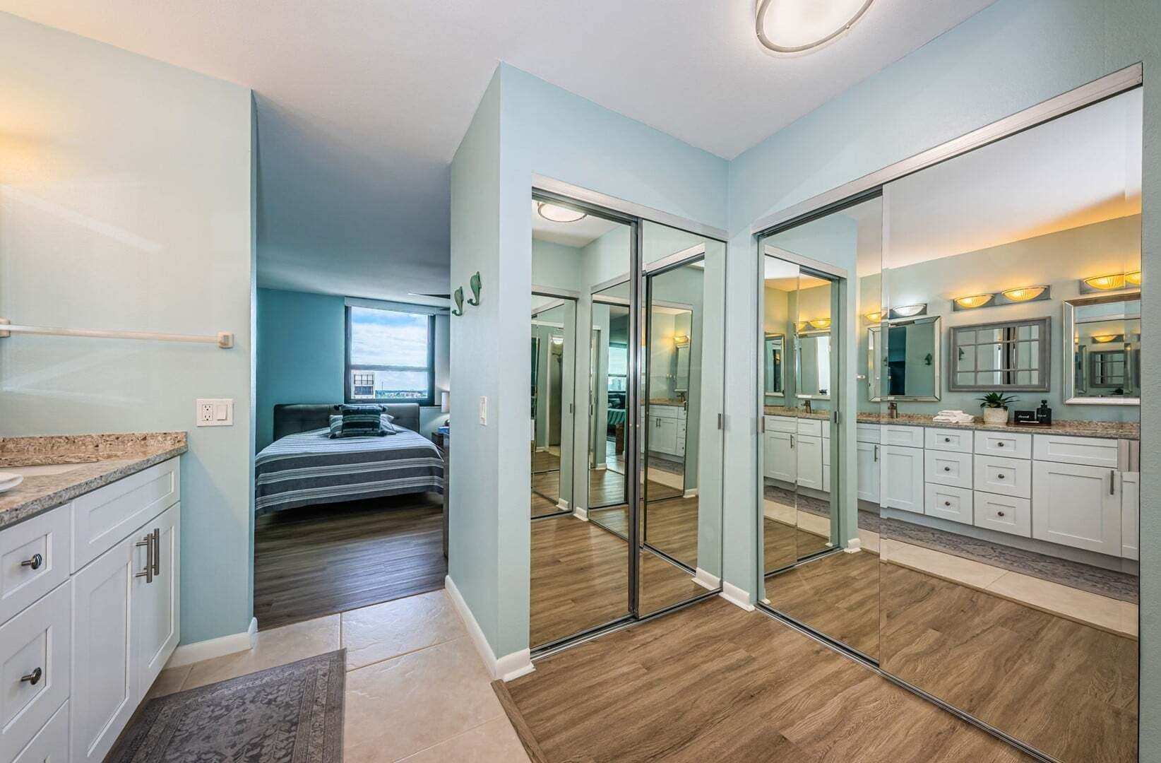 A hotel room with a bed, a bathroom with a large mirror, and a view of the city.