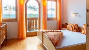 Ein Schlafzimmer mit einem hölzernen Bett, zwei mit Vorhängen versehenen Fenstern, Blick ins Freie und einem kleinen Balkon.