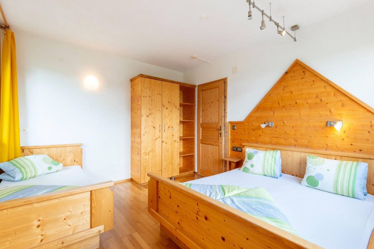 A room with two wooden beds, a wooden wardrobe, and a wooden ceiling with a sloped design.