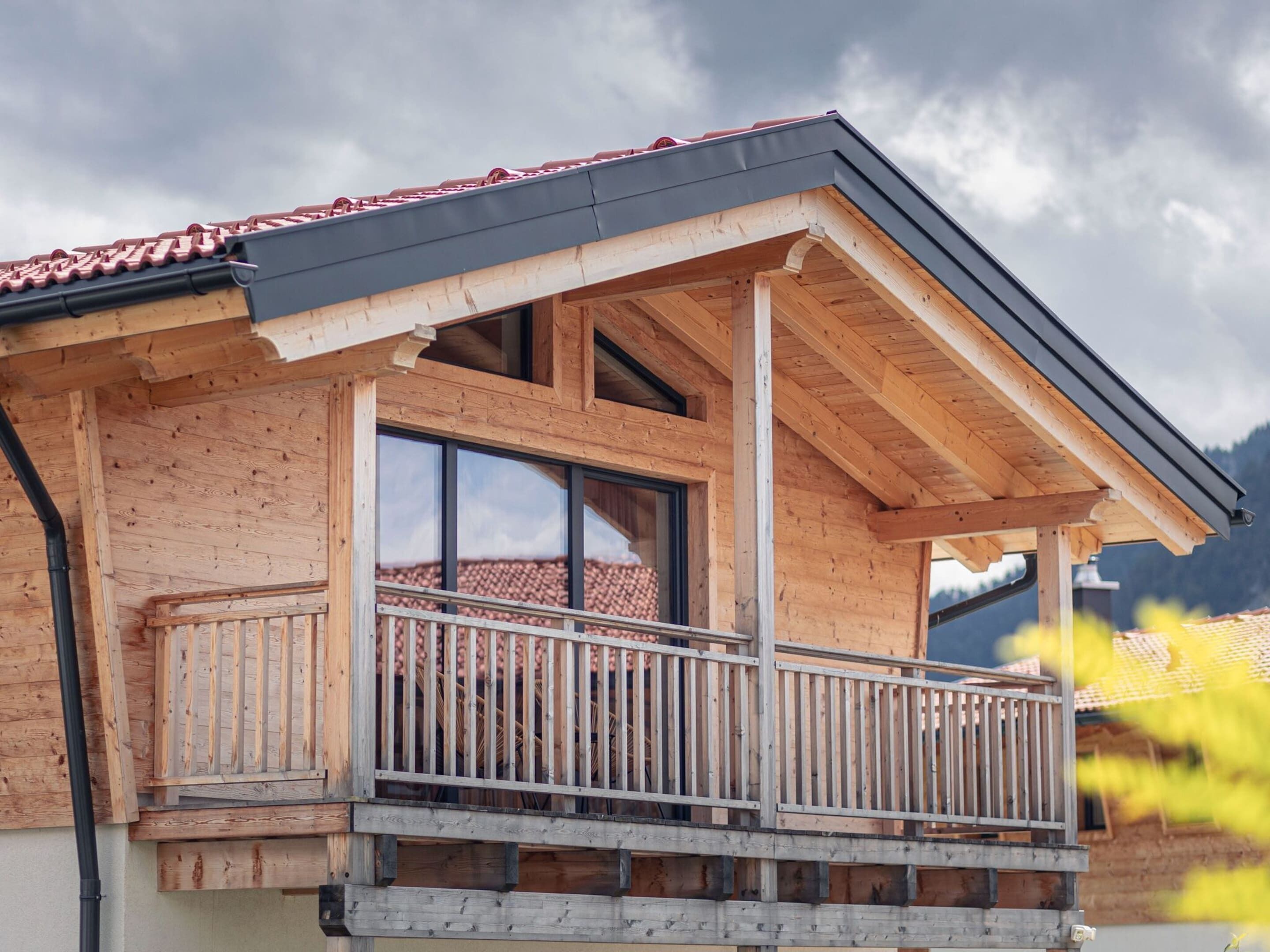 Ein Holzhaus mit Balkon, großen Fenstern und einem roten Ziegeldach.