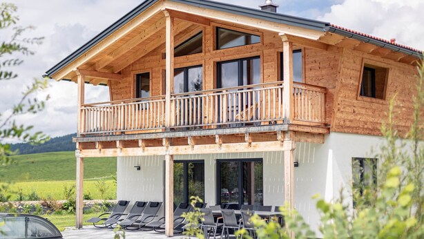 Een houten huis met twee verdiepingen, een balkon, een zwembad en buitenmeubels.
