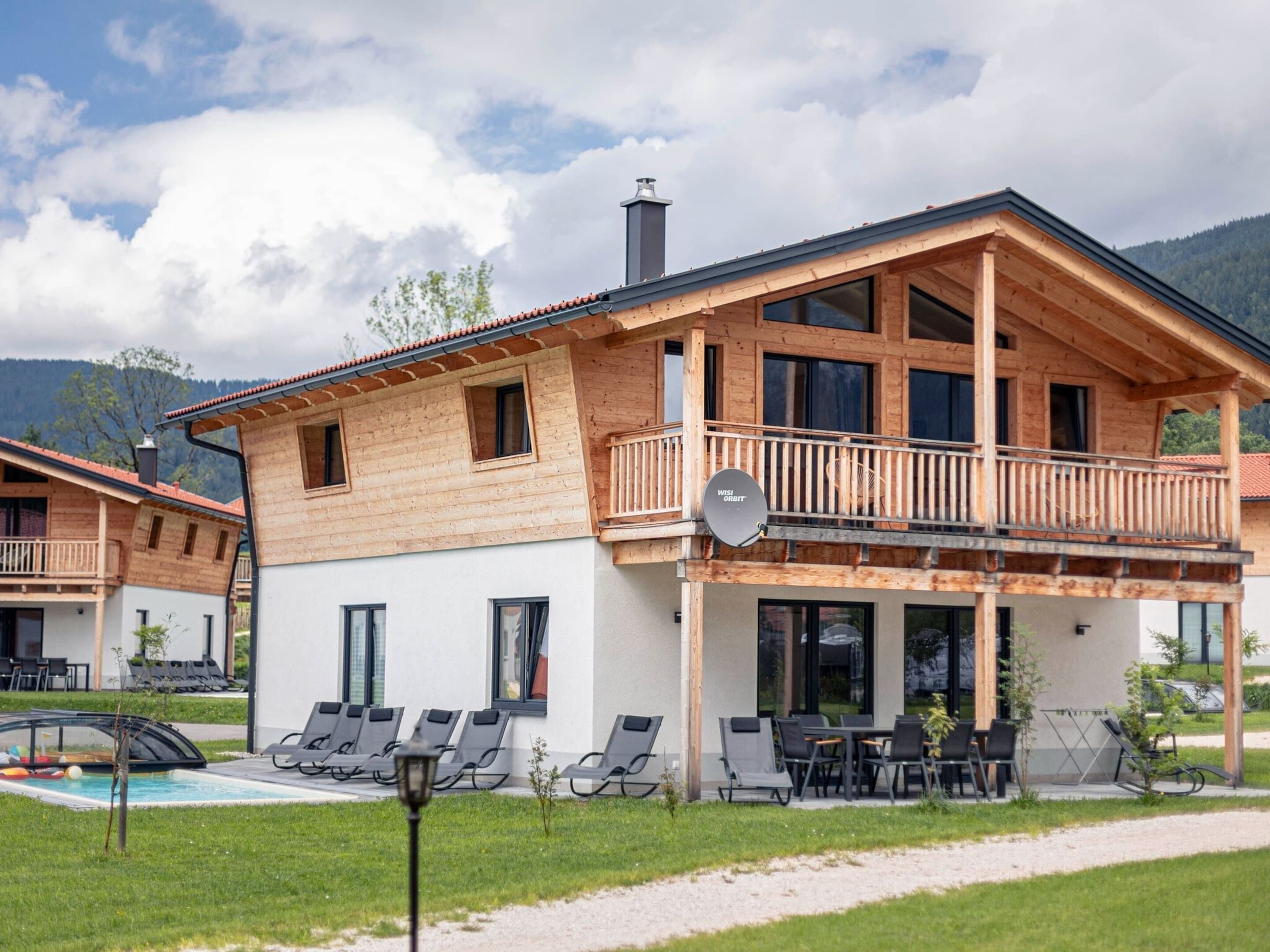 A wooden chalet with a balcony, a pool, and outdoor seating.
