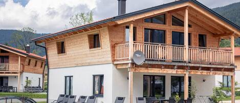 A wooden chalet with a balcony, a pool, and outdoor seating.