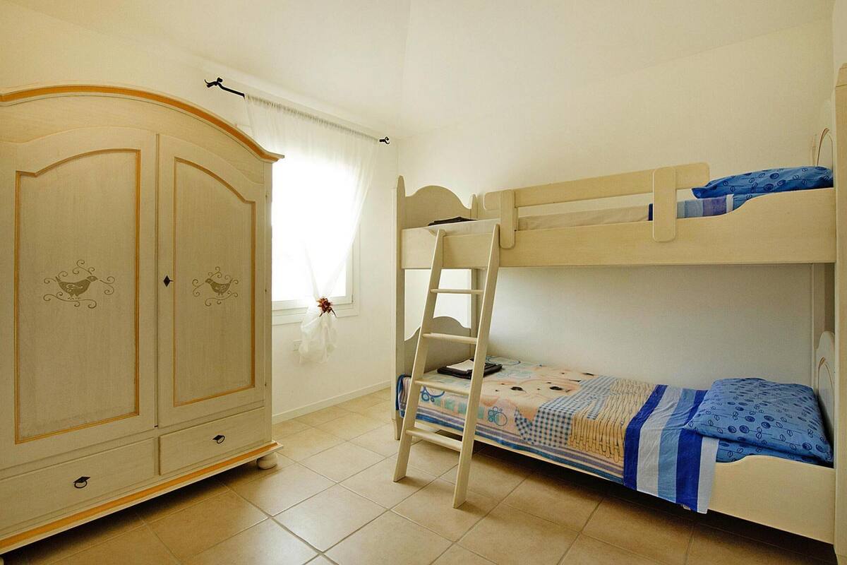 A bunk bed with a ladder, a wardrobe with decorative panels, and a window with curtains.